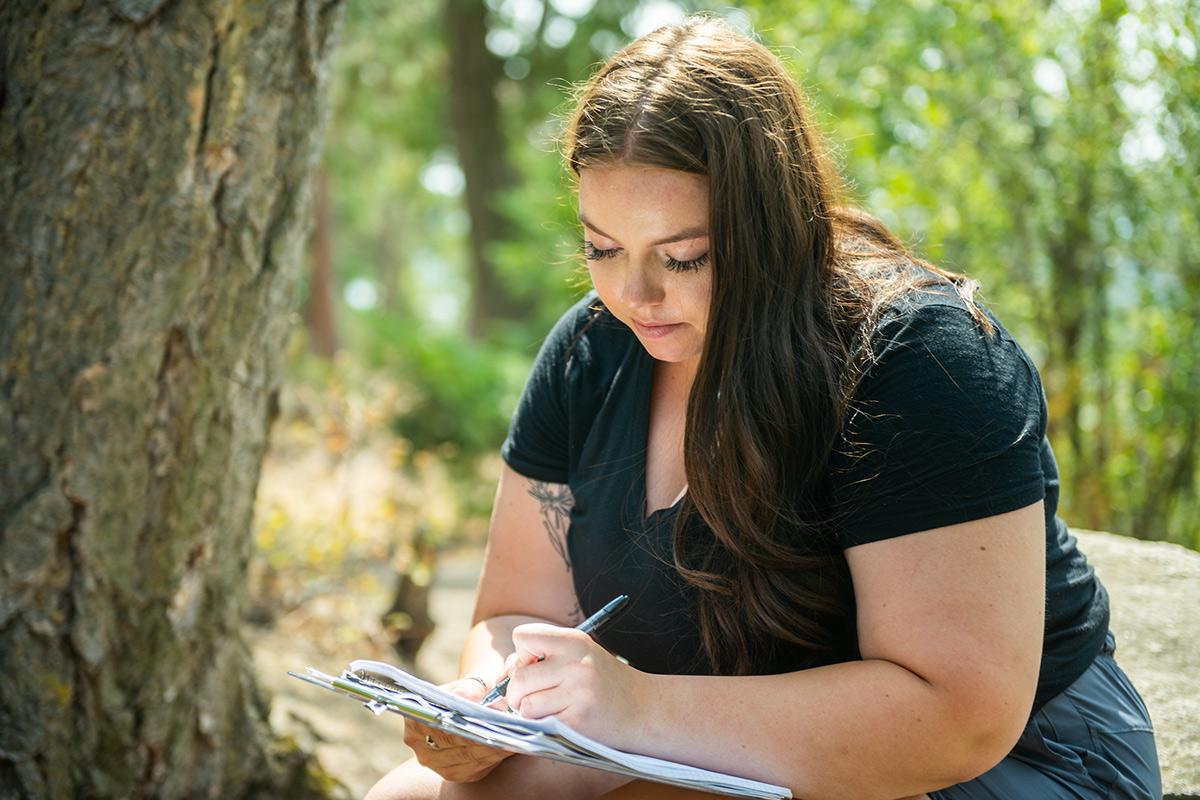艾玛·阿曼在森林里的一棵树旁做笔记.